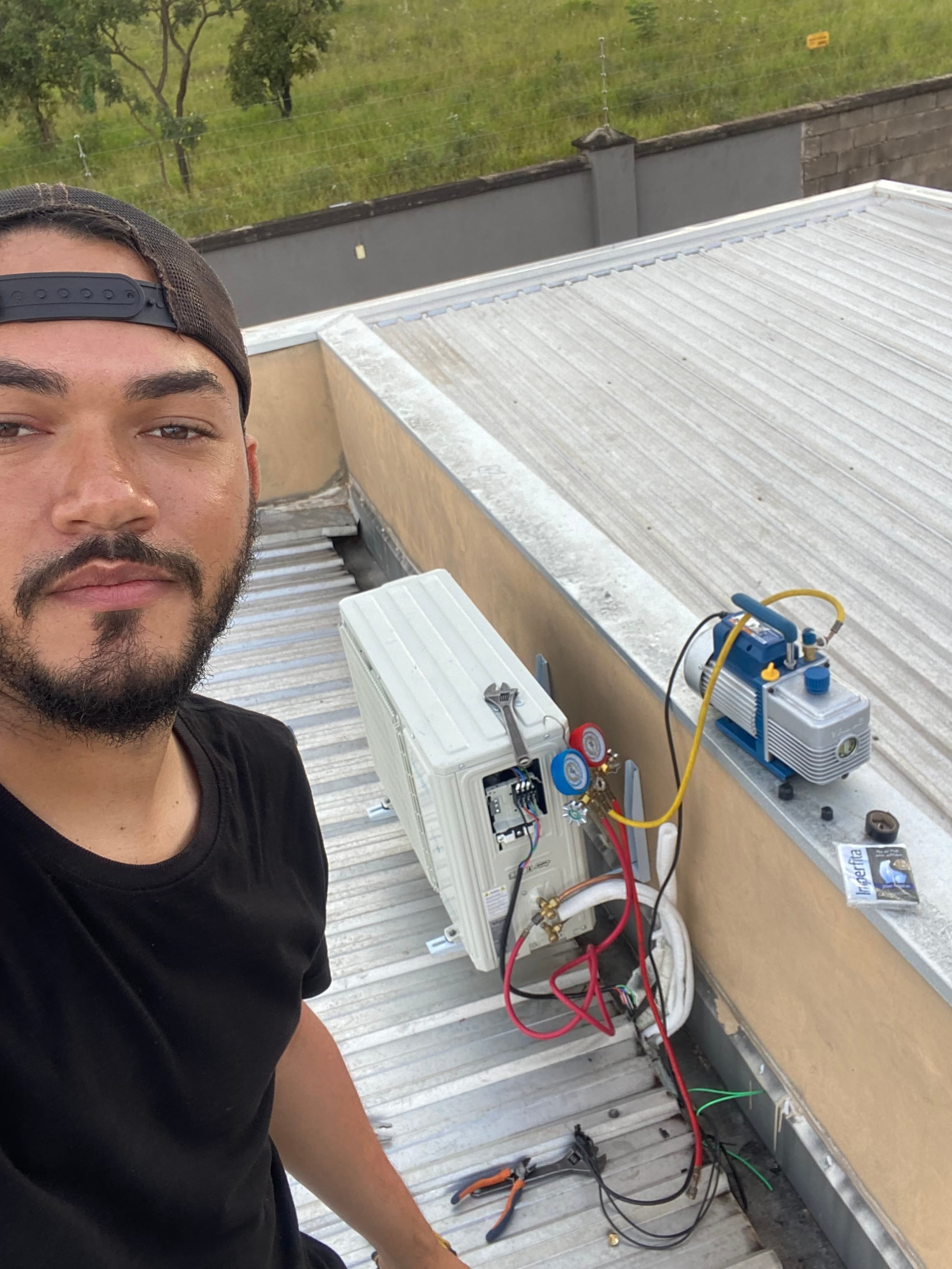 Técnico instalando ar-condicionado em telhado com bomba de vácuo, manômetros e ferramentas de refrigeração.