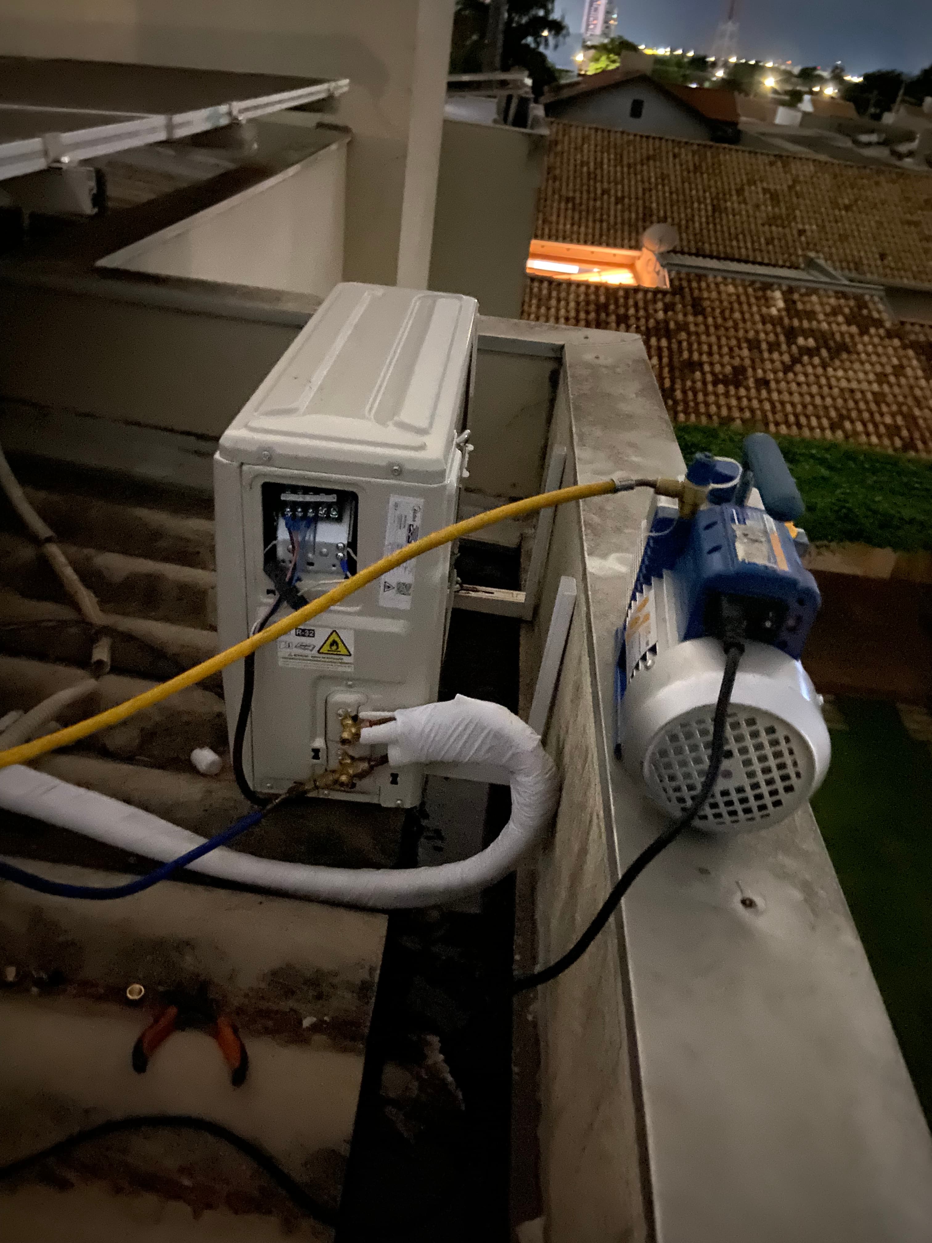 Bomba de vácuo azul conectada por mangueira amarela a uma unidade externa de ar-condicionado.