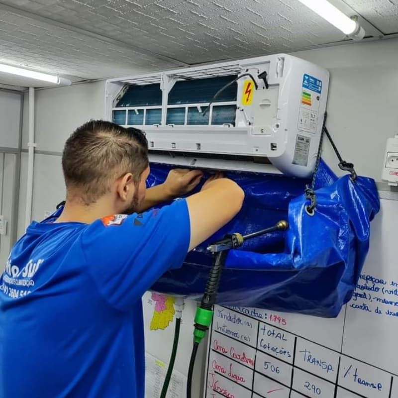 Técnico limpa unidade interna de ar-condicionado split usando bolsa coletora azul para manutenção.